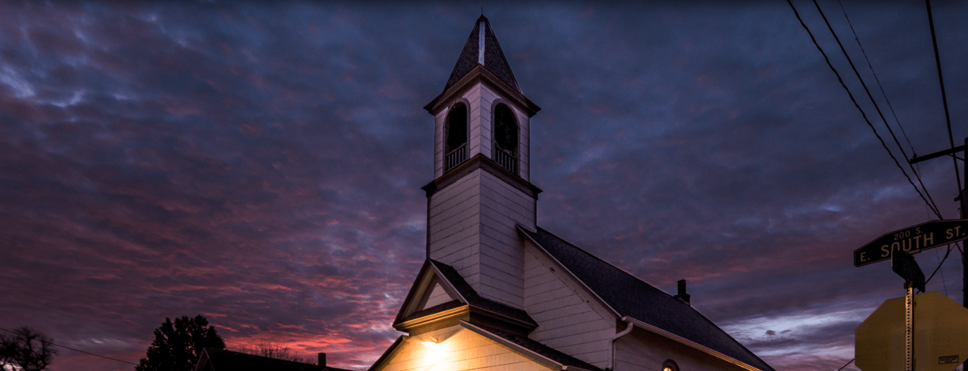 A small white church with a steeple is lit up at night.