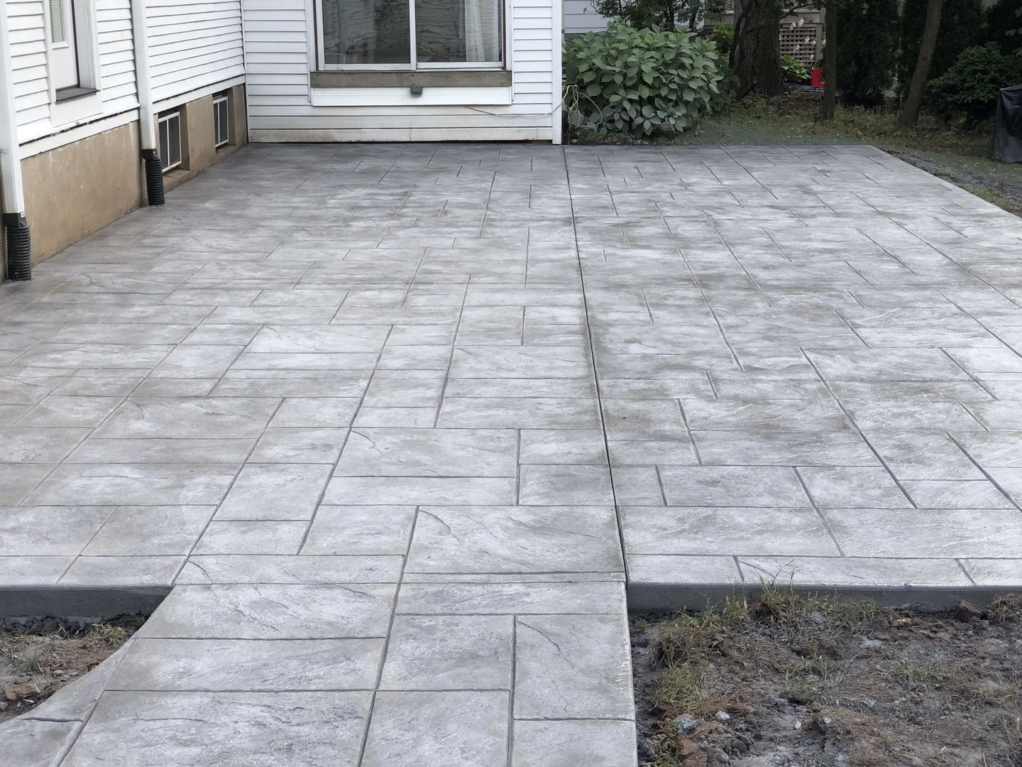 A concrete walkway leading to a house with a white house in the background.