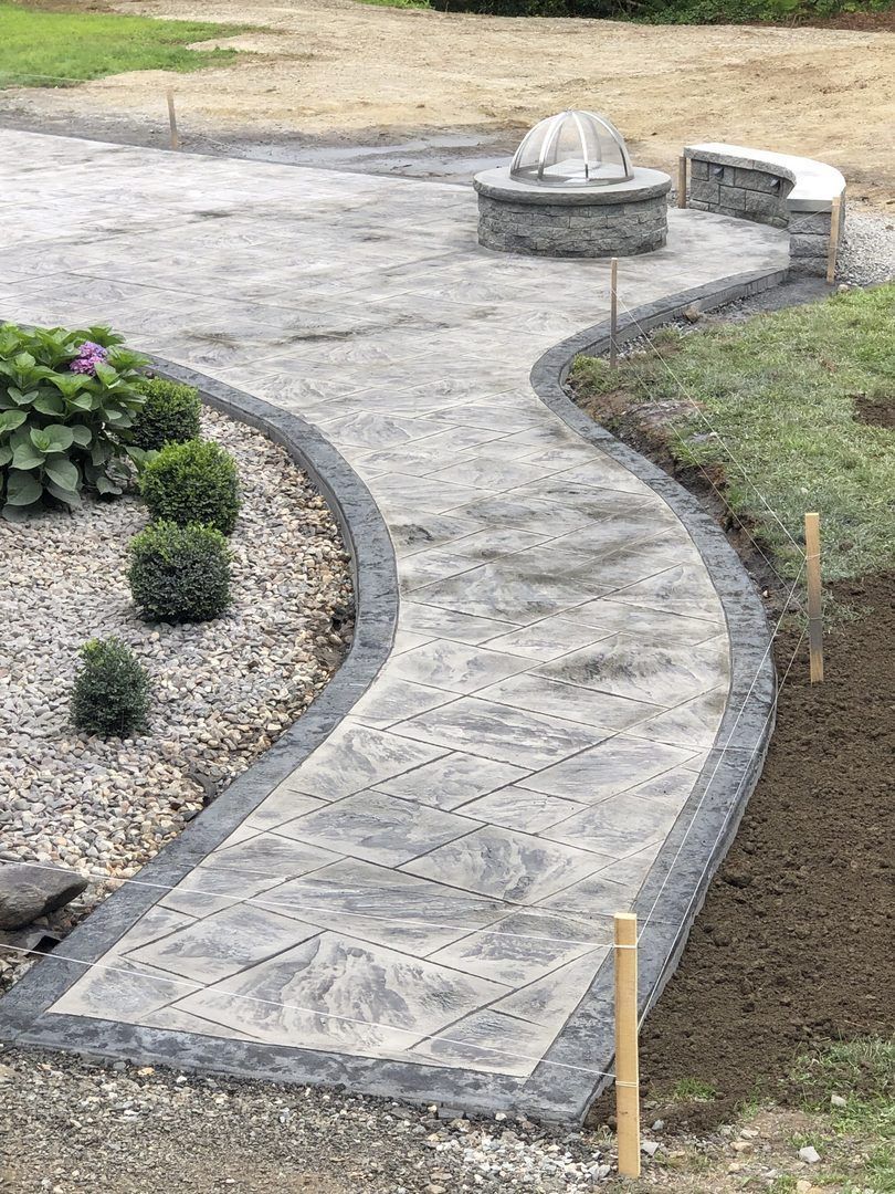 A concrete walkway leading to a fire pit in a backyard.