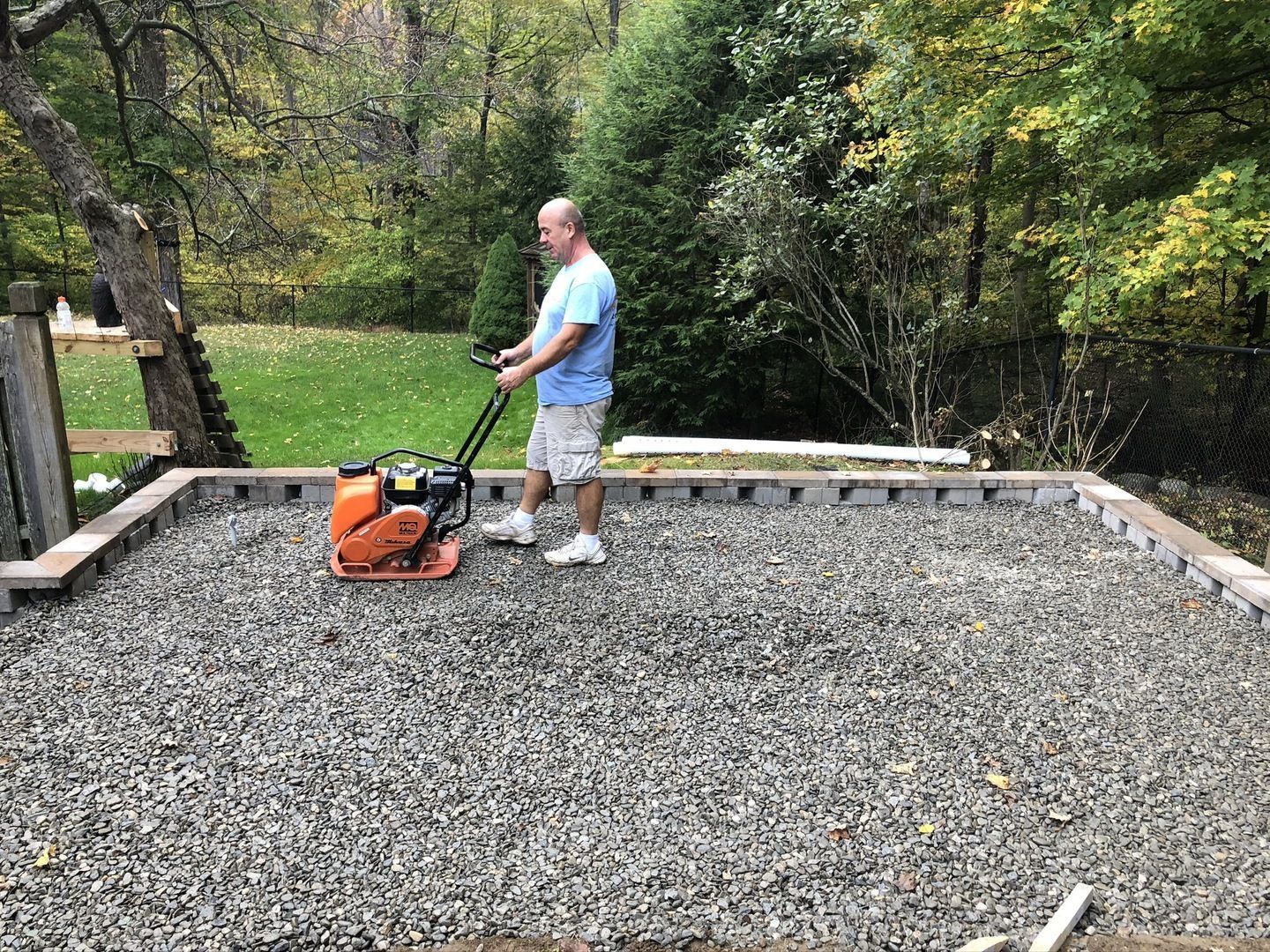 A man is using a vibratory plate to level a gravel area.