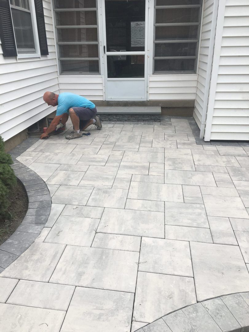 A man is kneeling on a patio in front of a house.