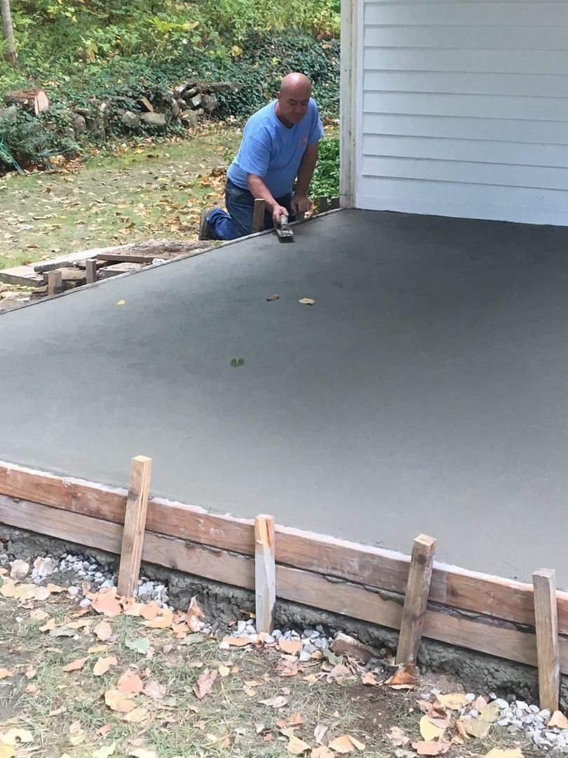 A man is kneeling on the ground working on a concrete floor.