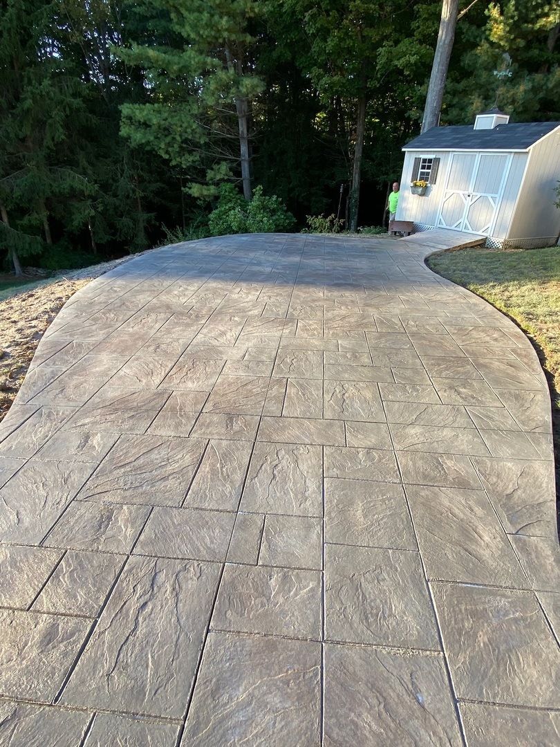 A concrete walkway leading to a house with trees in the background.
