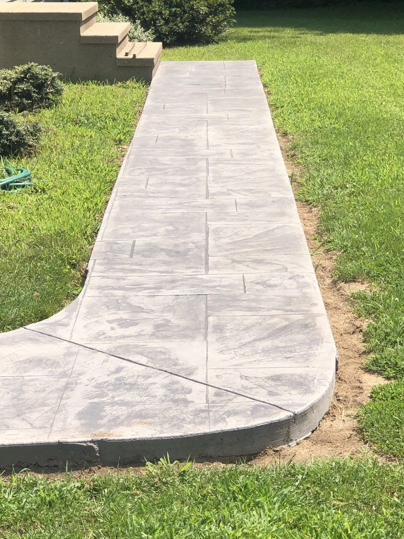 A concrete walkway going through a lush green yard.