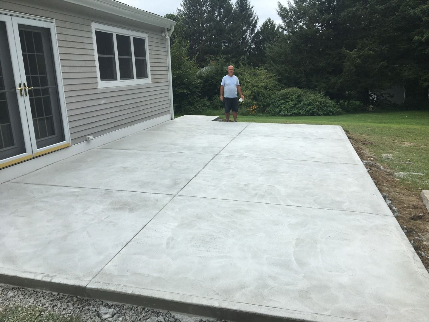 A man is standing on a concrete patio in front of a house.