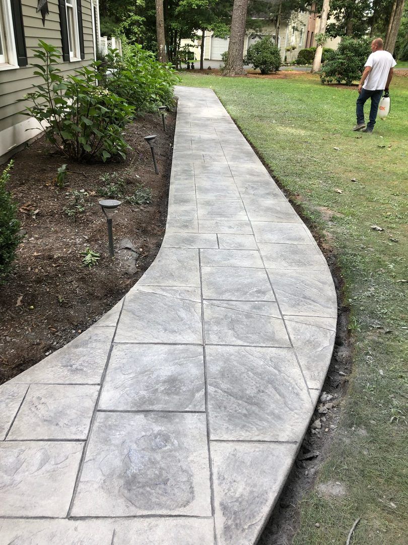A man is walking down a concrete walkway in front of a house.