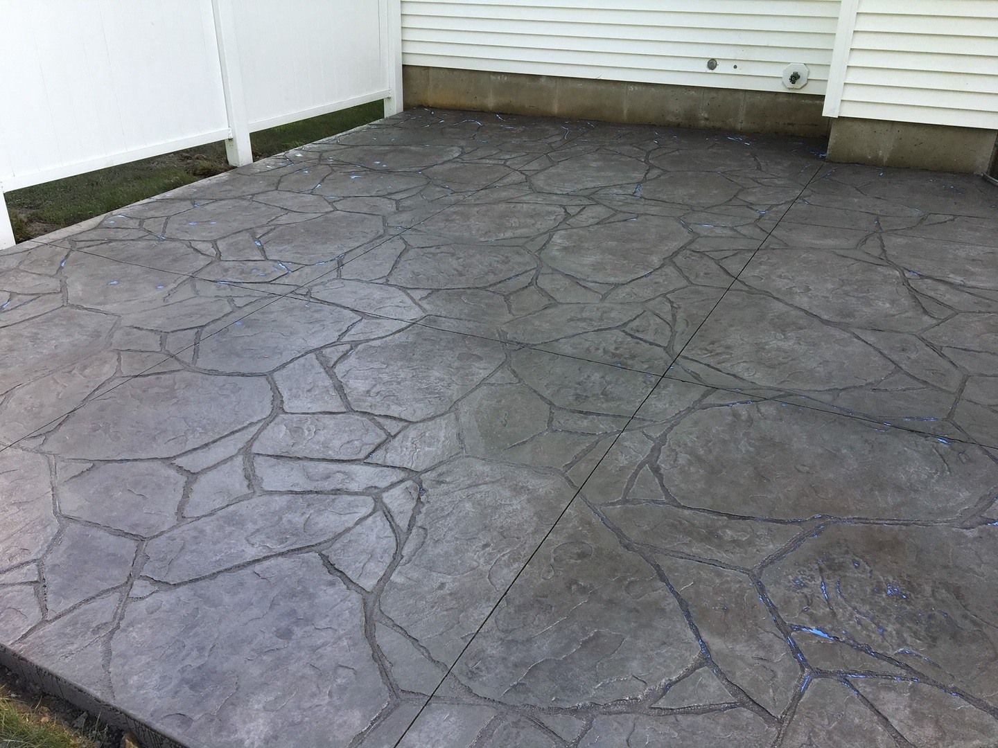 A concrete patio with a white fence in the background.