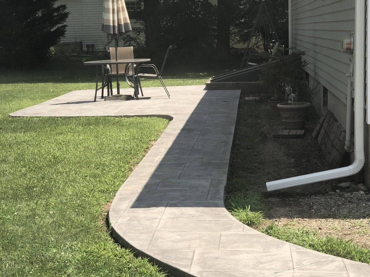A concrete walkway leading to a patio with a table and chairs.