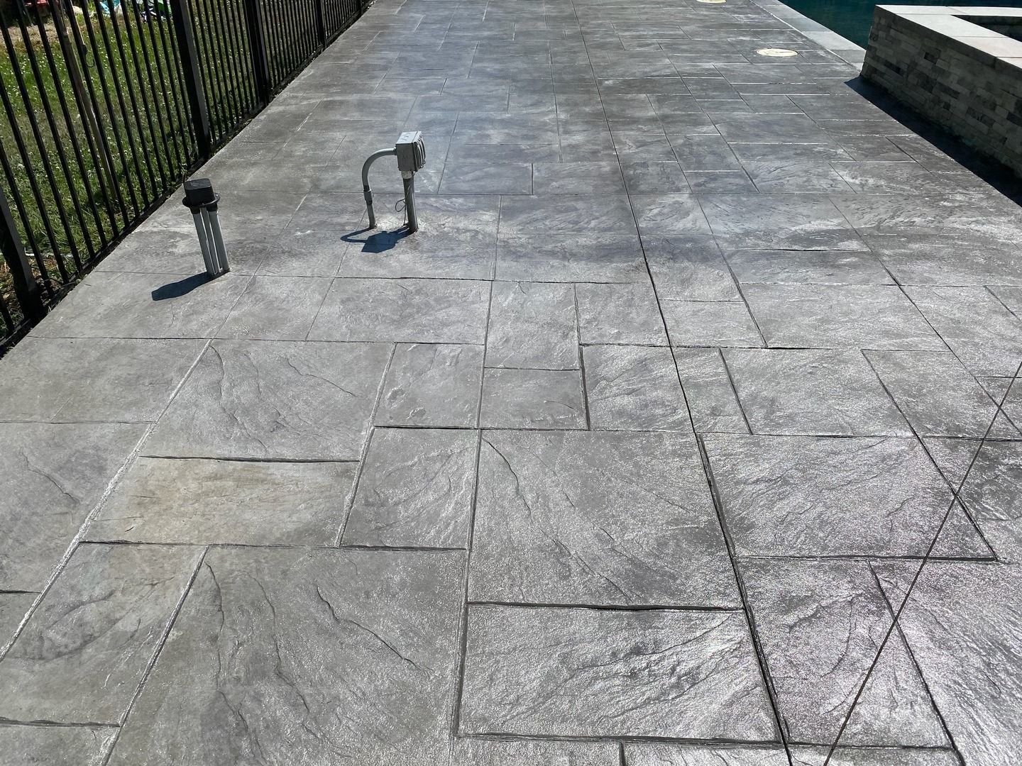 A concrete walkway leading to a pool next to a fence.