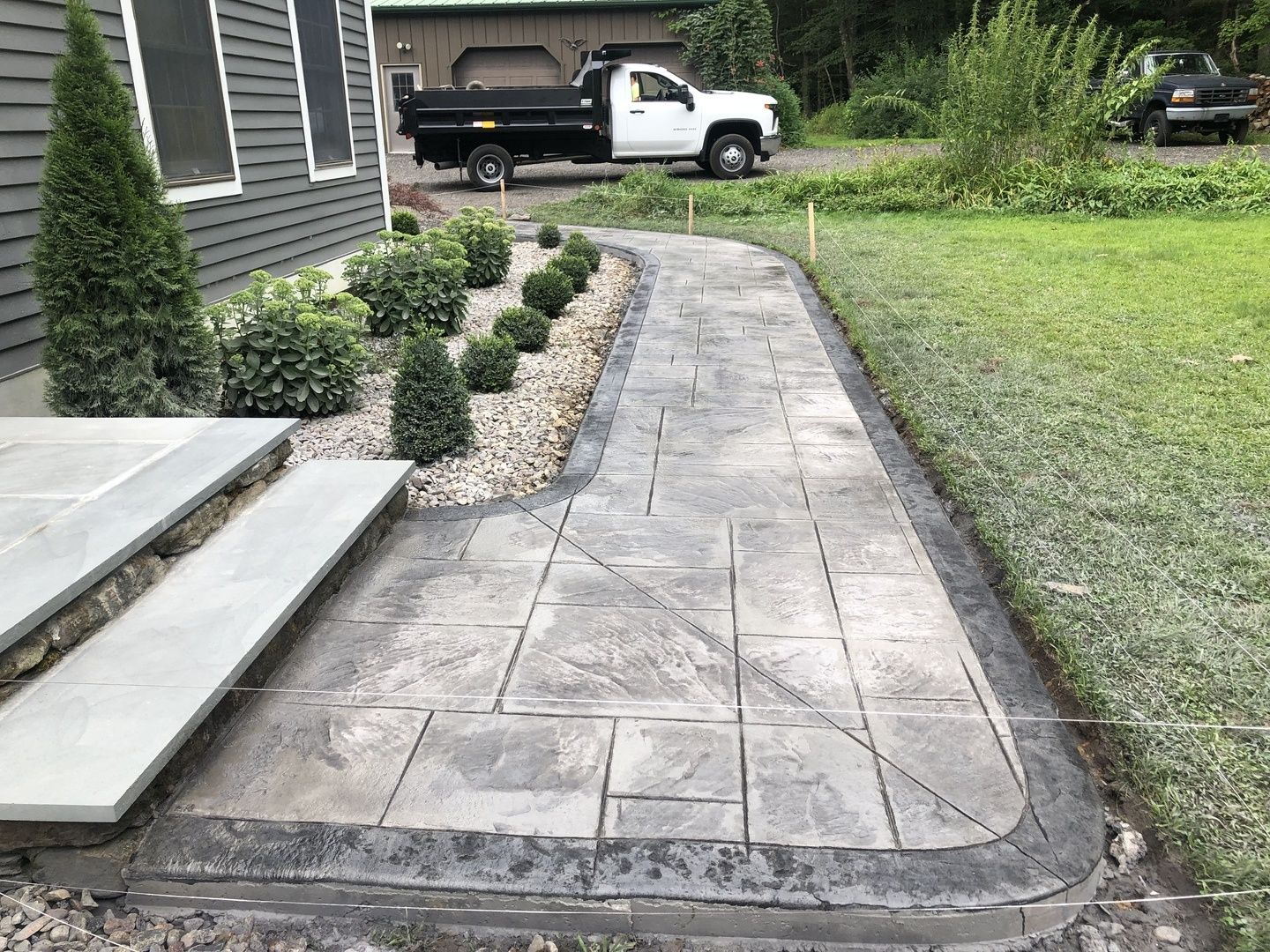 A white truck is parked on the side of the road next to a concrete walkway.