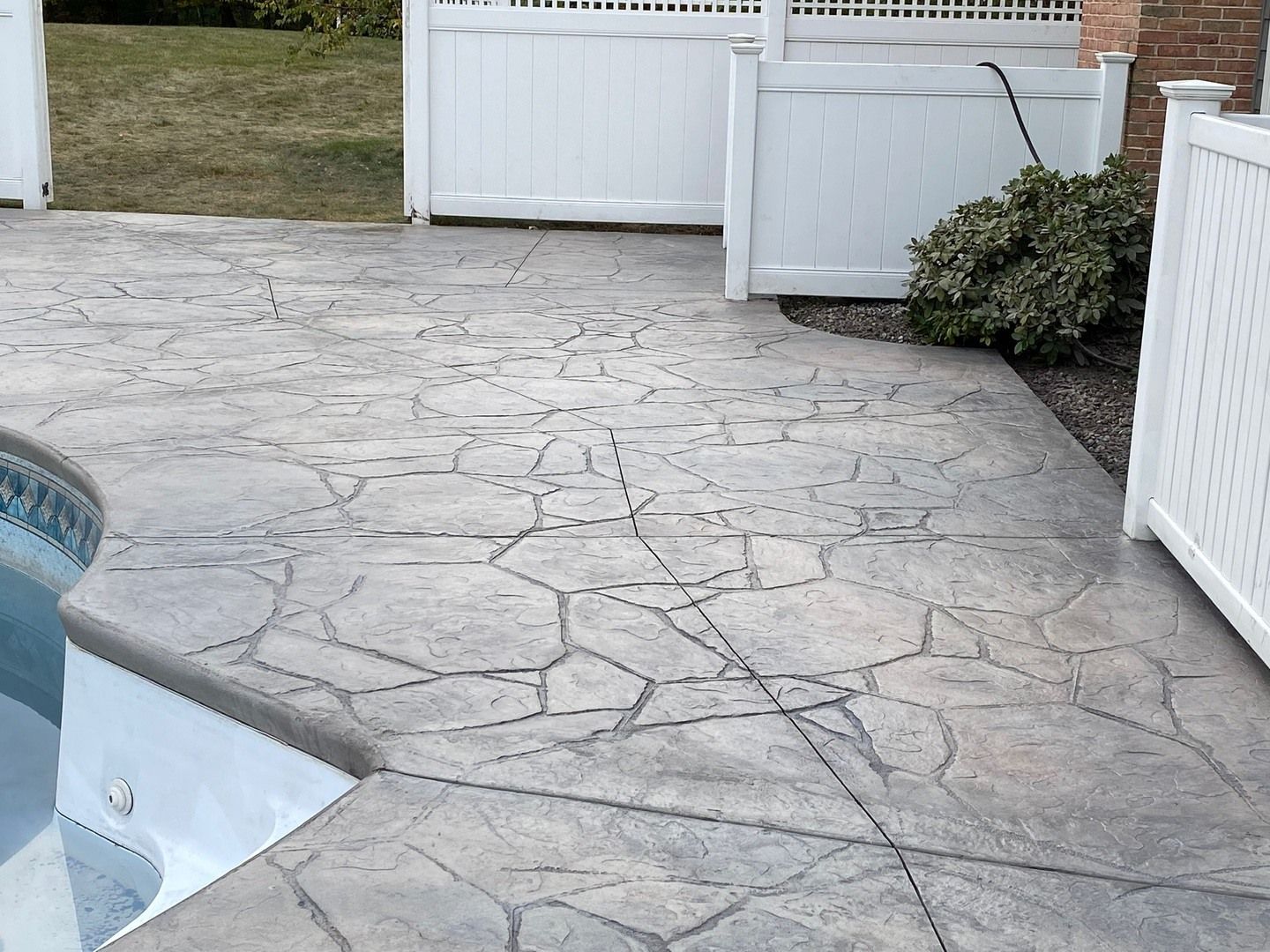 A concrete patio next to a pool with a white fence.