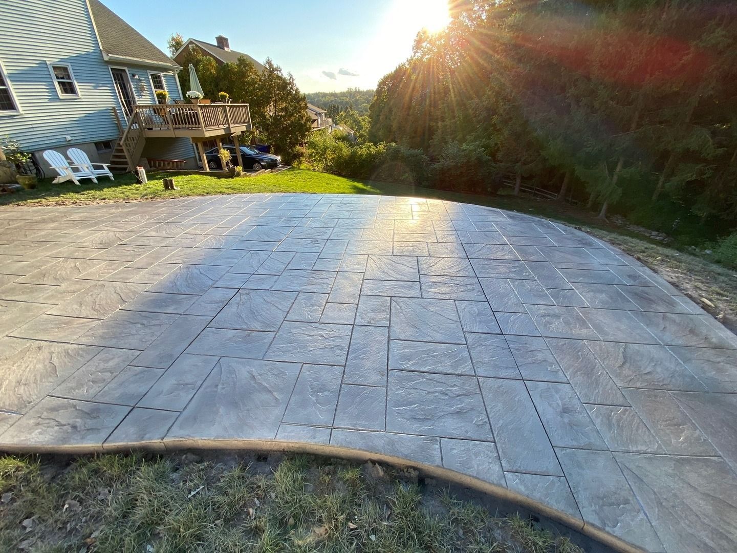 A concrete driveway with a house in the background and the sun shining through the trees.