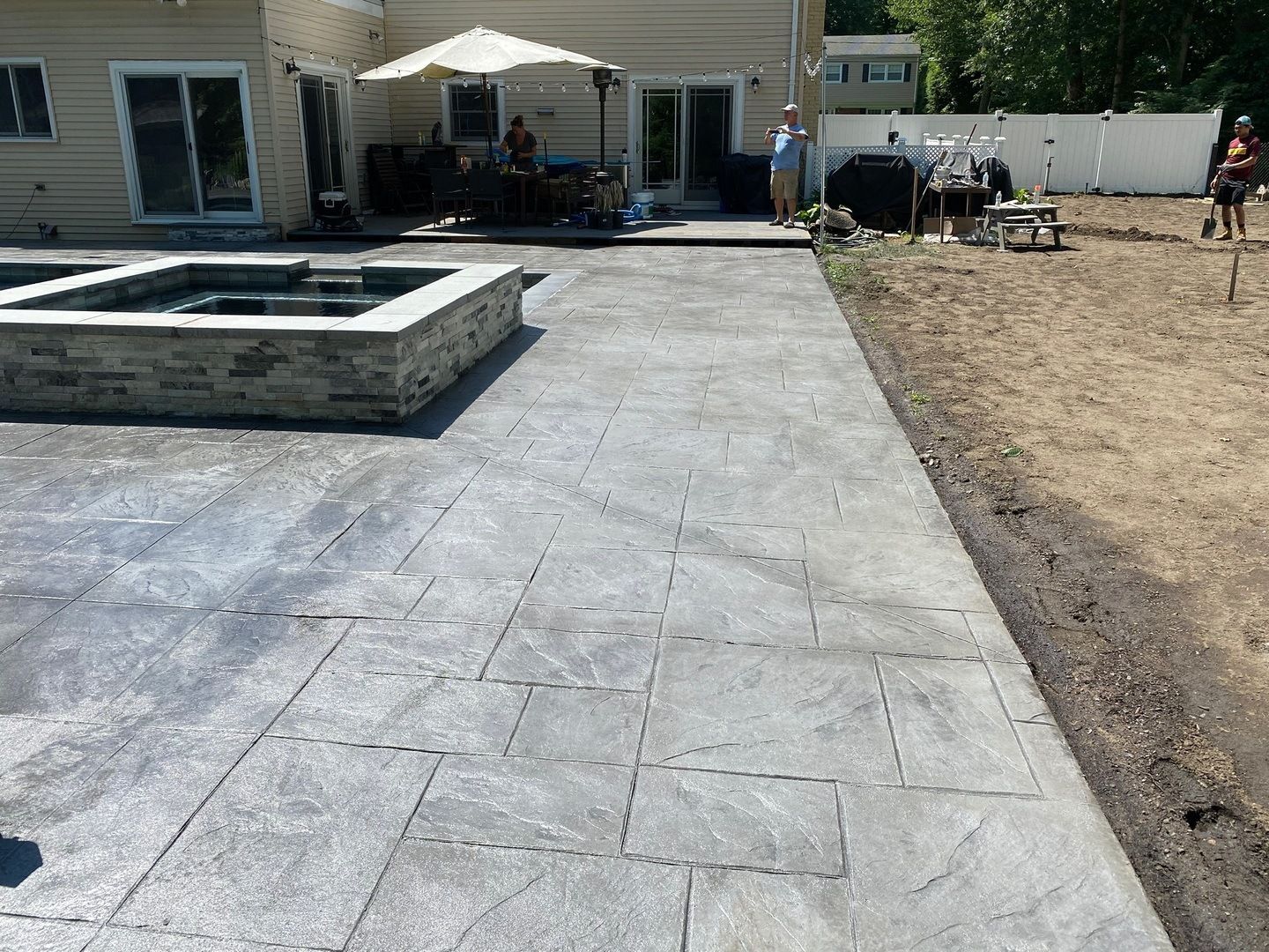 A patio with a fire pit in the middle of it and a house in the background.
