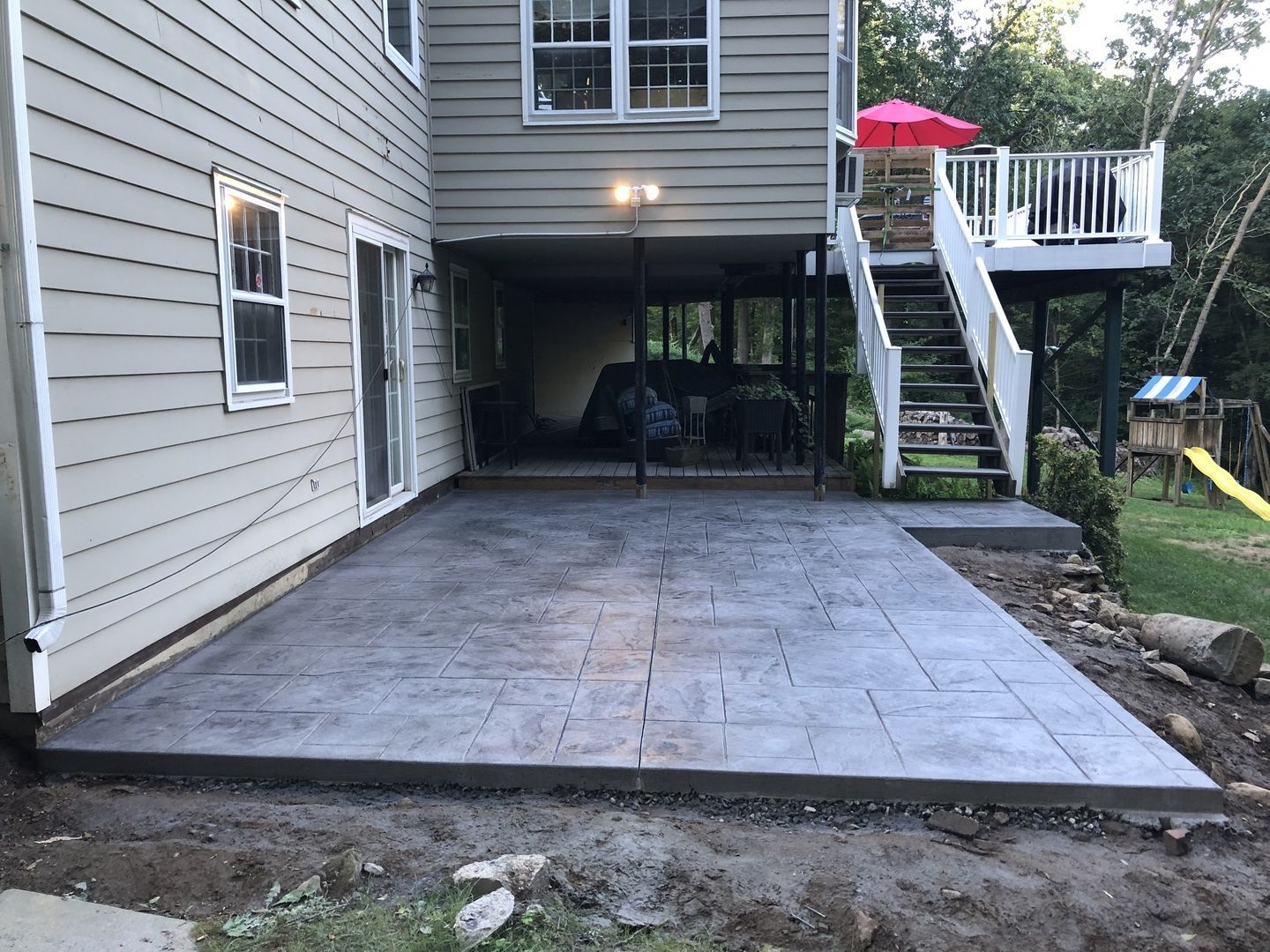 The backyard of a house with a patio and stairs leading to the deck.