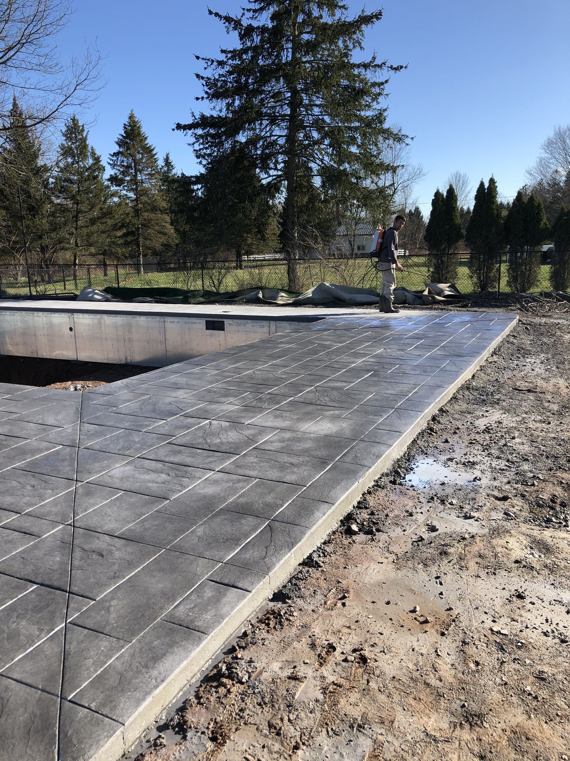 A man is standing on a concrete walkway next to a pool.