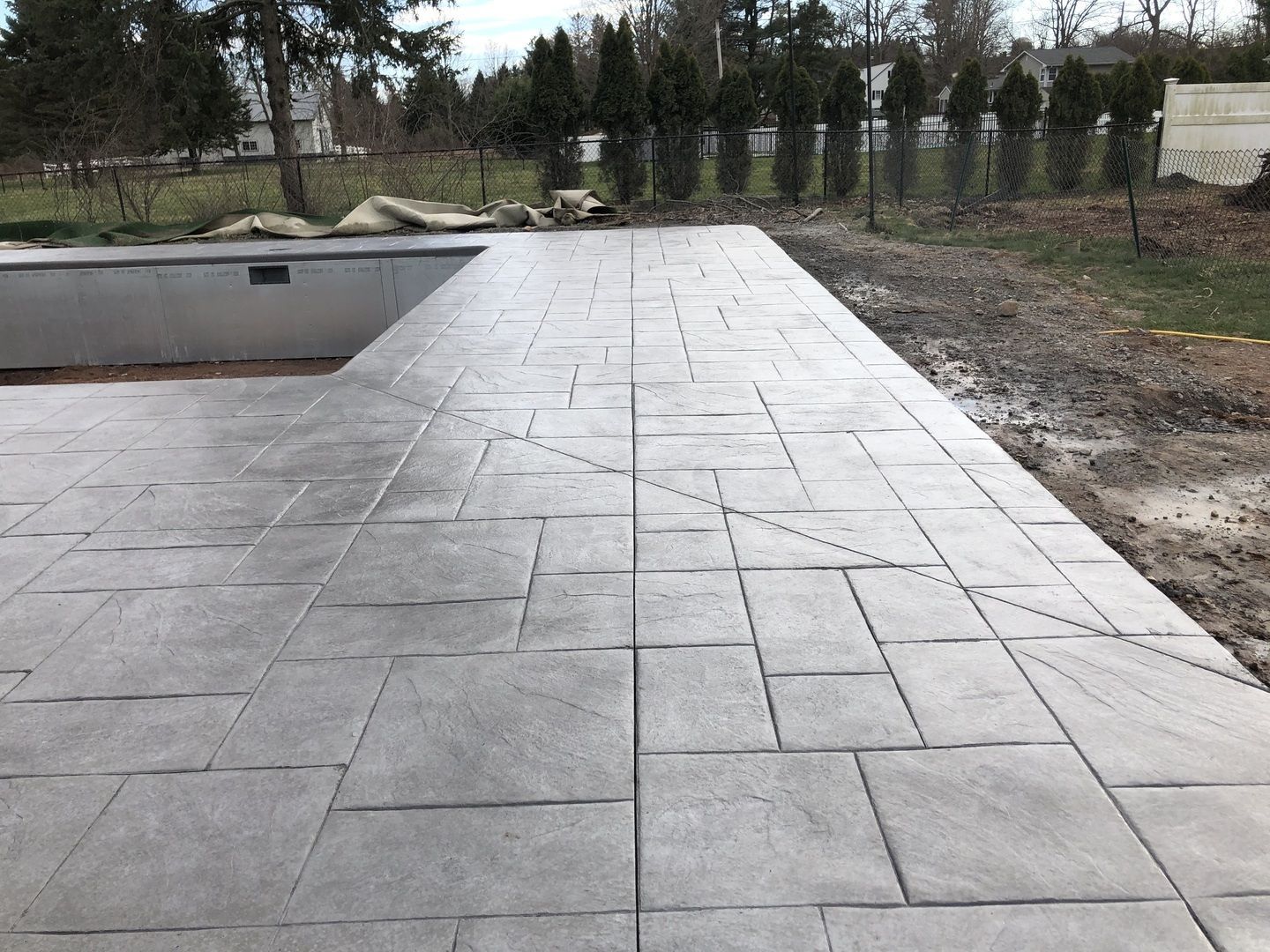 A concrete walkway leading to a pool with trees in the background