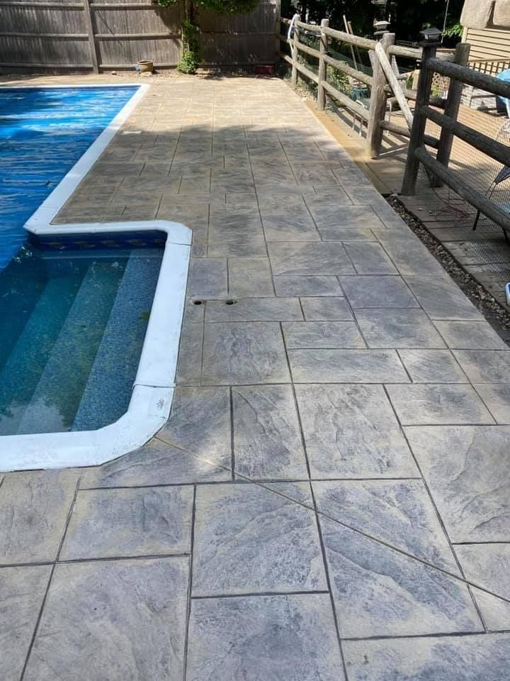 A concrete patio next to a swimming pool with stairs leading to it.