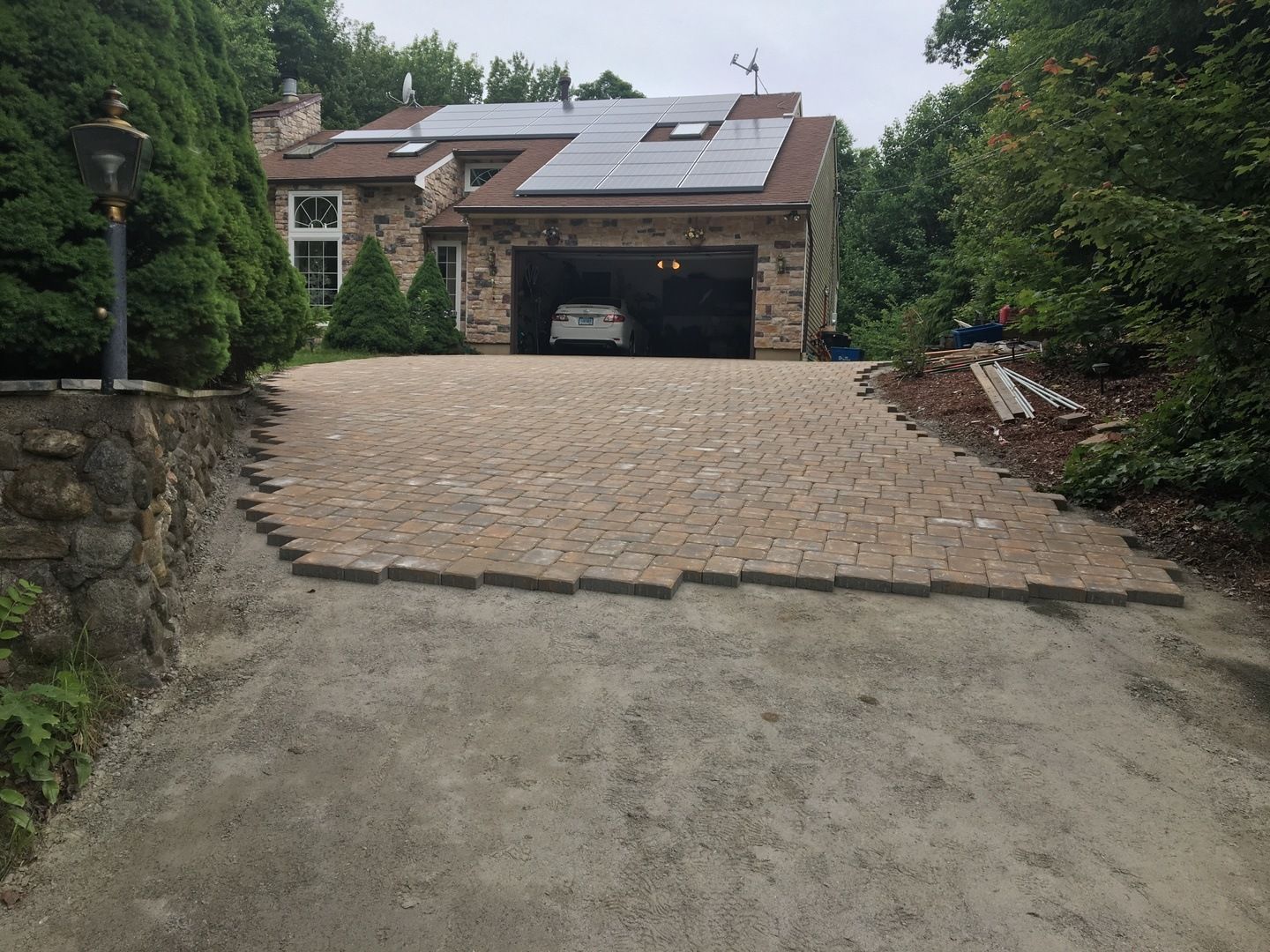 A car is parked in the driveway of a house with solar panels on the roof.