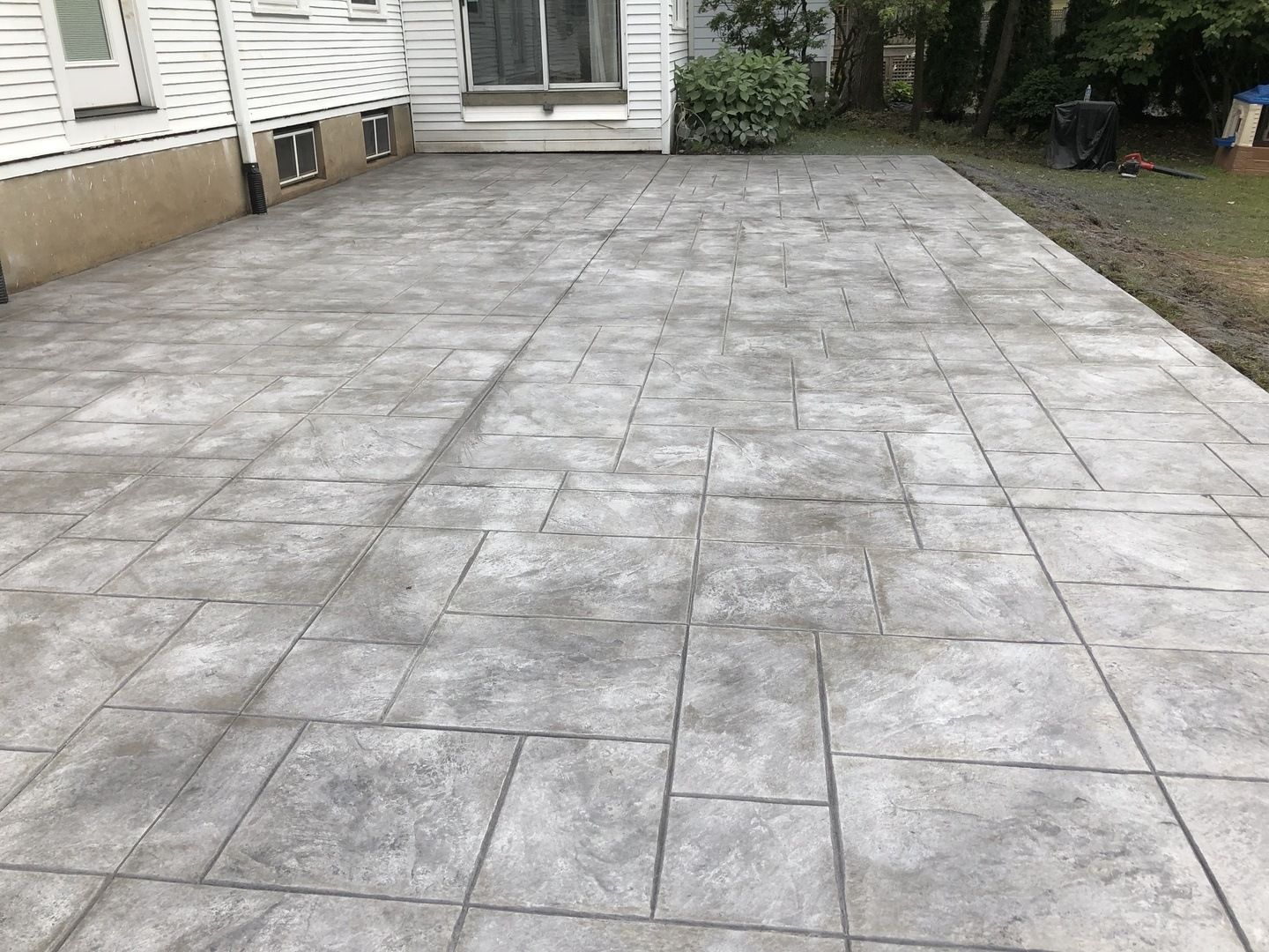 A concrete patio in front of a house with a sliding glass door.