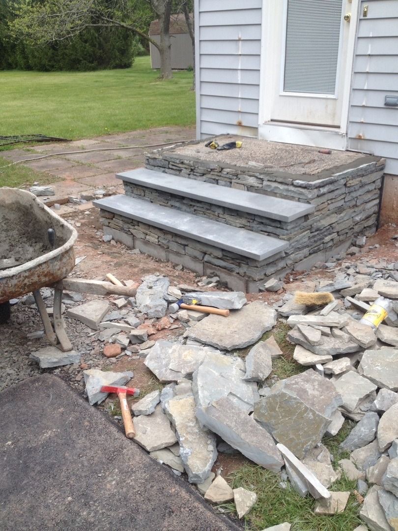 A wheelbarrow is sitting next to a set of stairs being built in front of a house.