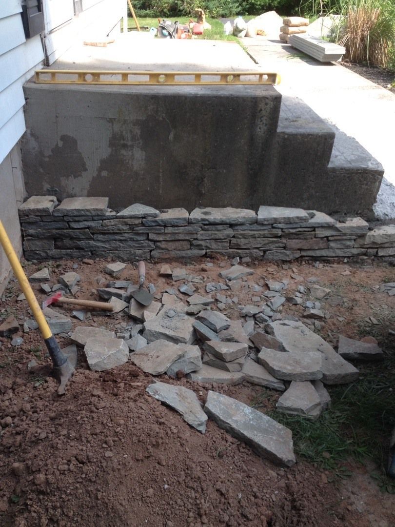 A shovel is in the dirt in front of a stone wall