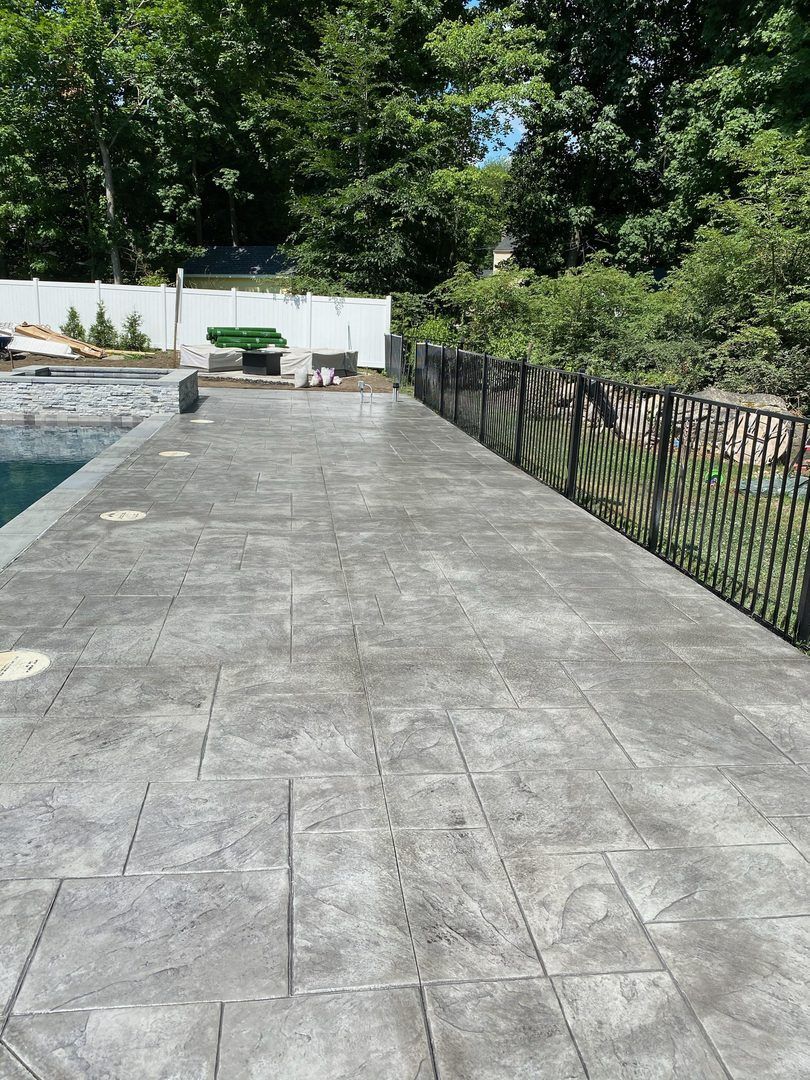 A patio with a fence and a pool in the background.