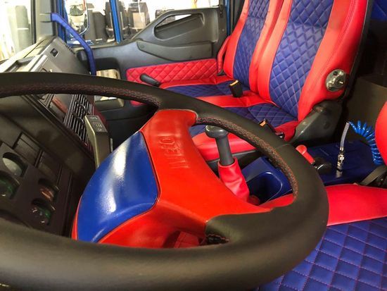 L'interno di un camion con sedili rossi e blu e un volante.
