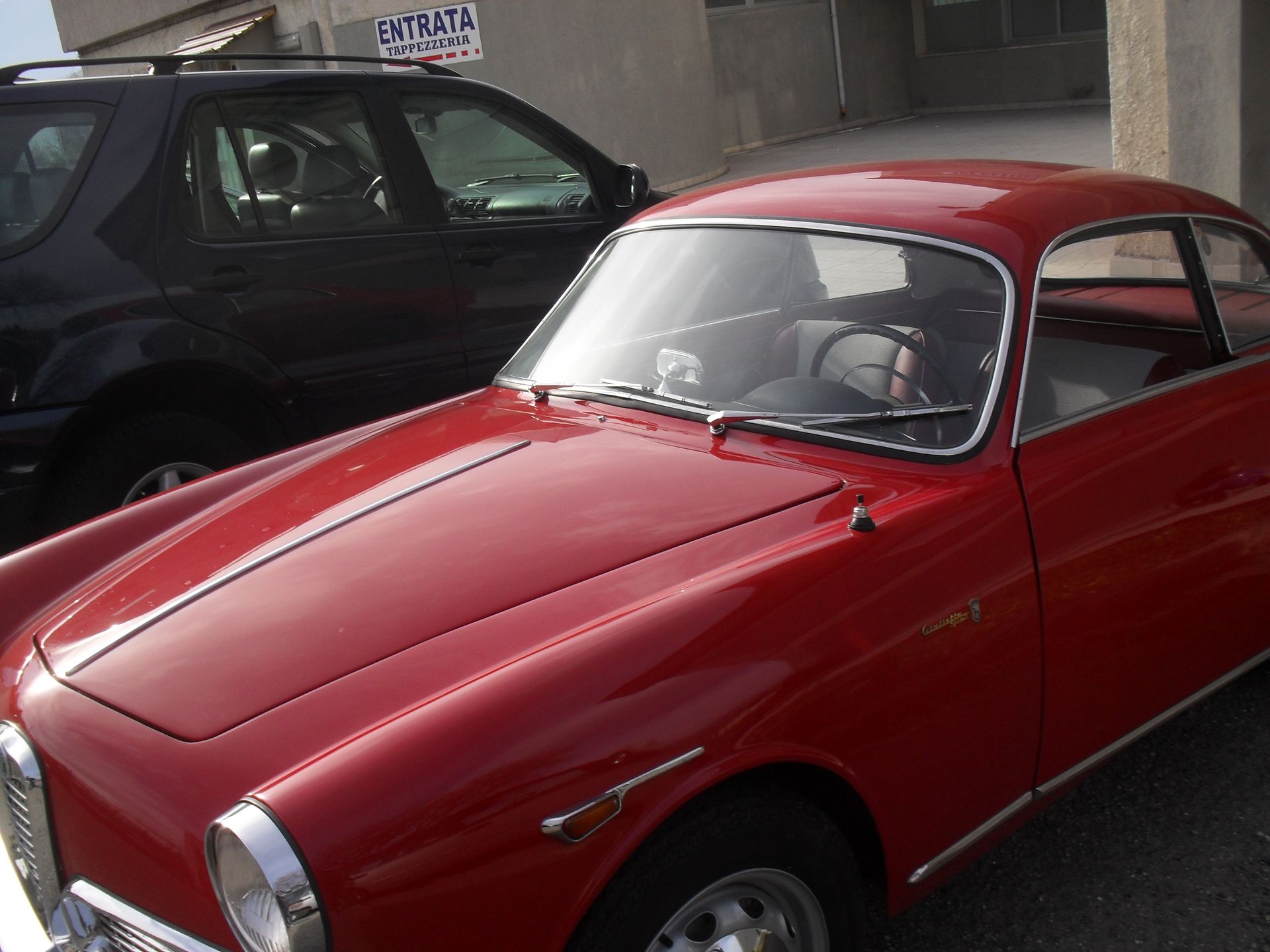 Un'auto rossa è parcheggiata davanti a un cartello che dice entrata
