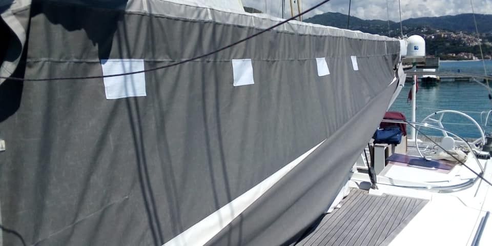 Una barca a vela con una copertura grigia sul lato è ormeggiata in un porto.