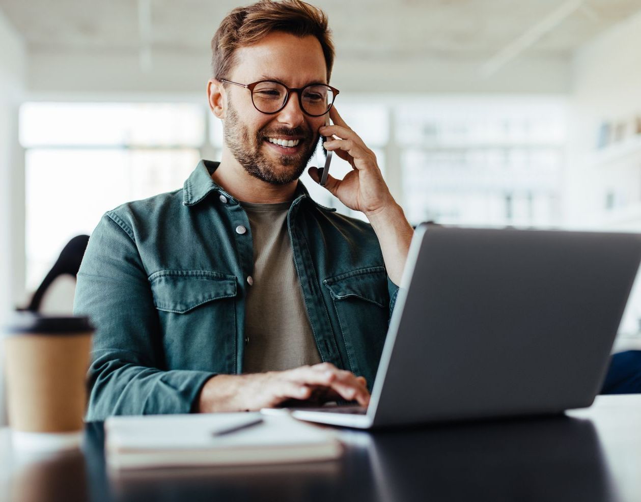 Een man praat op een mobiele telefoon terwijl hij een laptopcomputer gebruikt.