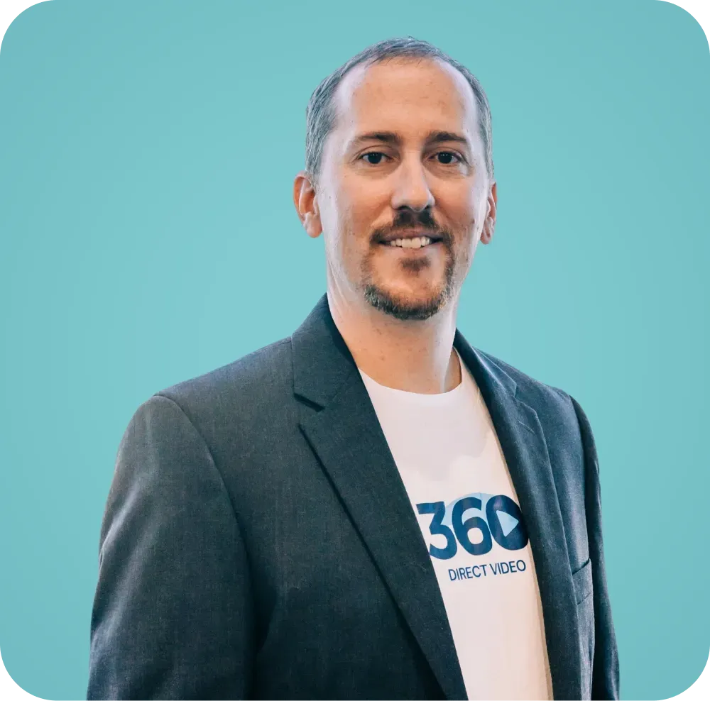 A man in a suit and a t-shirt with the word 360 on it is standing in front of a blue background.