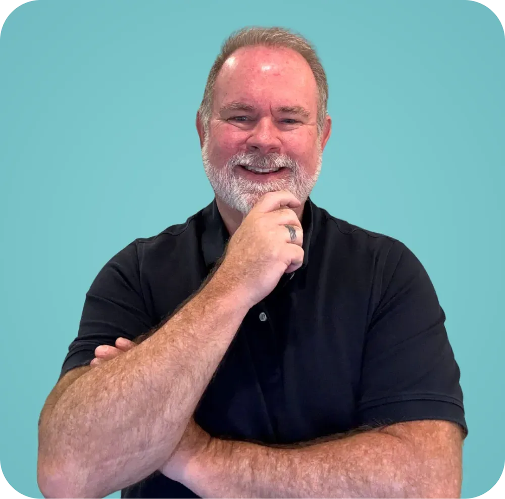A man with a beard is smiling with his arms crossed and his hand on his chin.