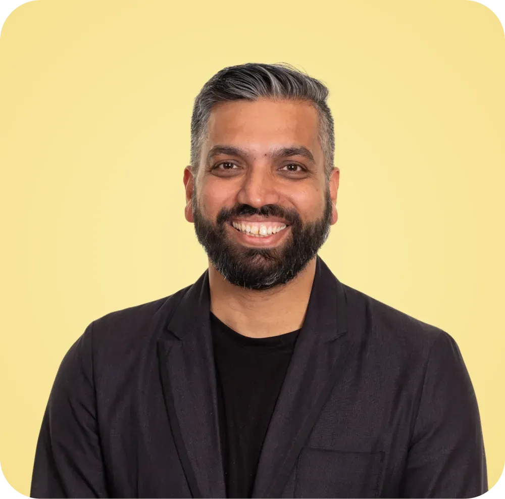 A man with a beard is wearing a black jacket and smiling.