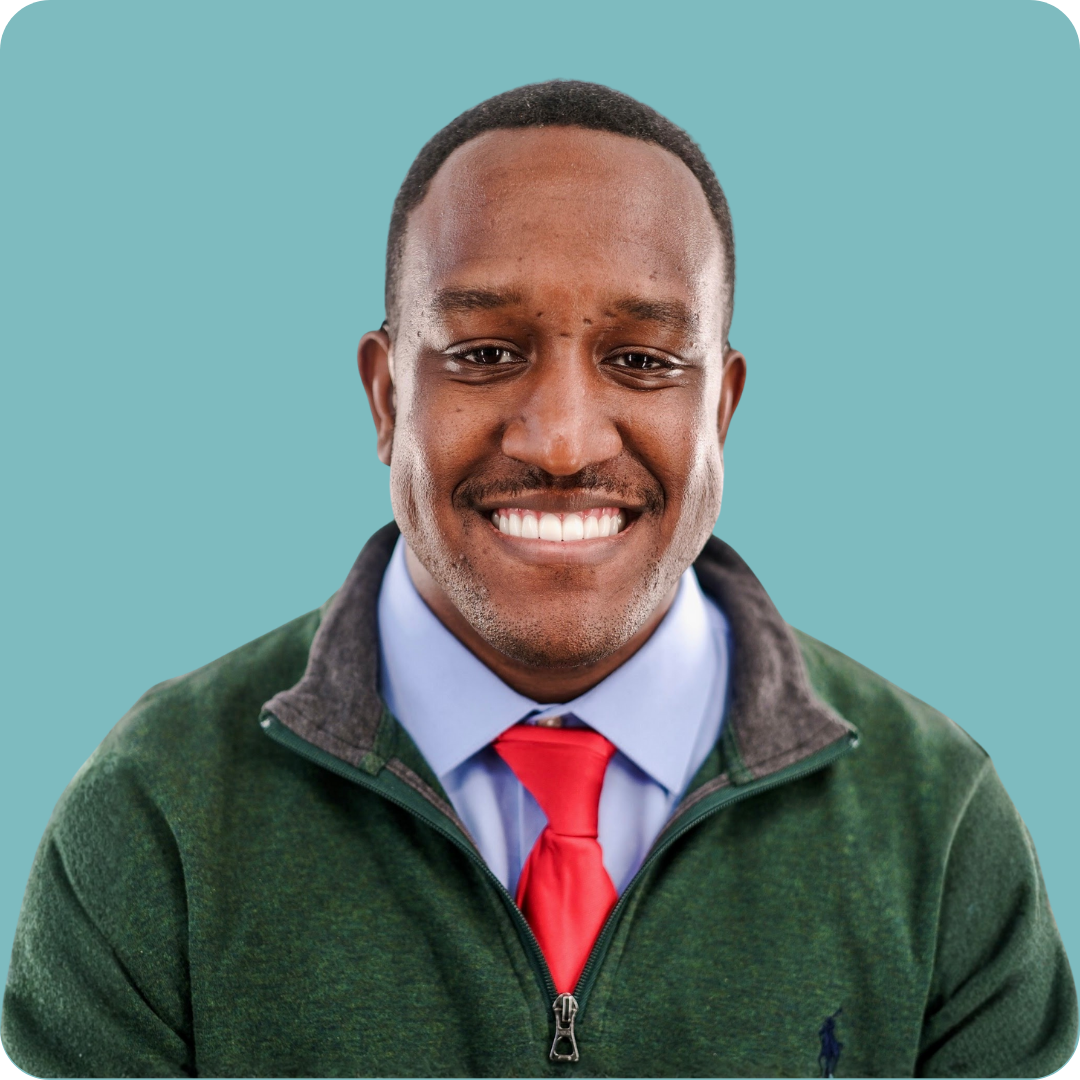 A man is wearing a light blue shirt, red tie, and green sweater.