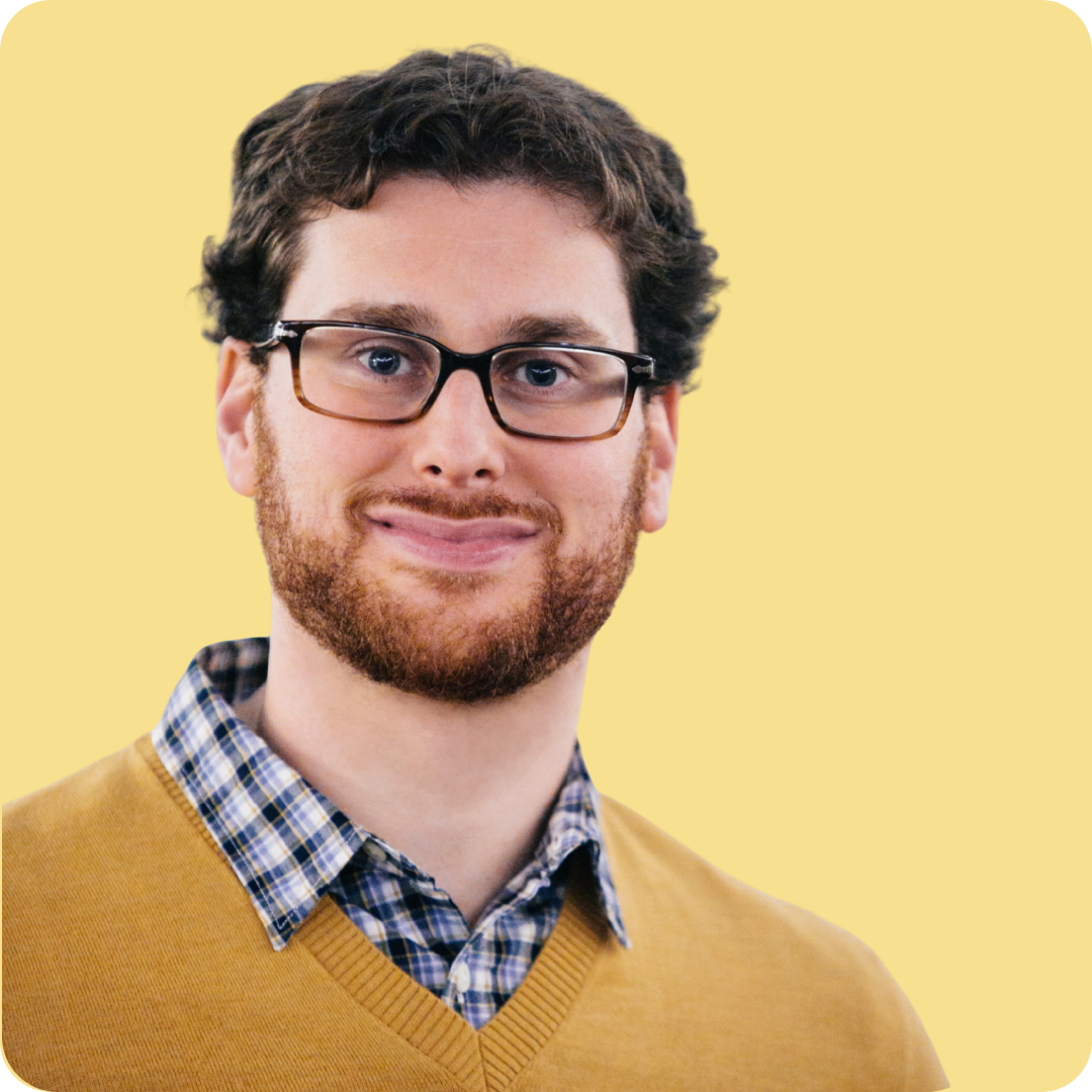 A man is wearing a blue plaid shirt with a yellow v-neck sweater.