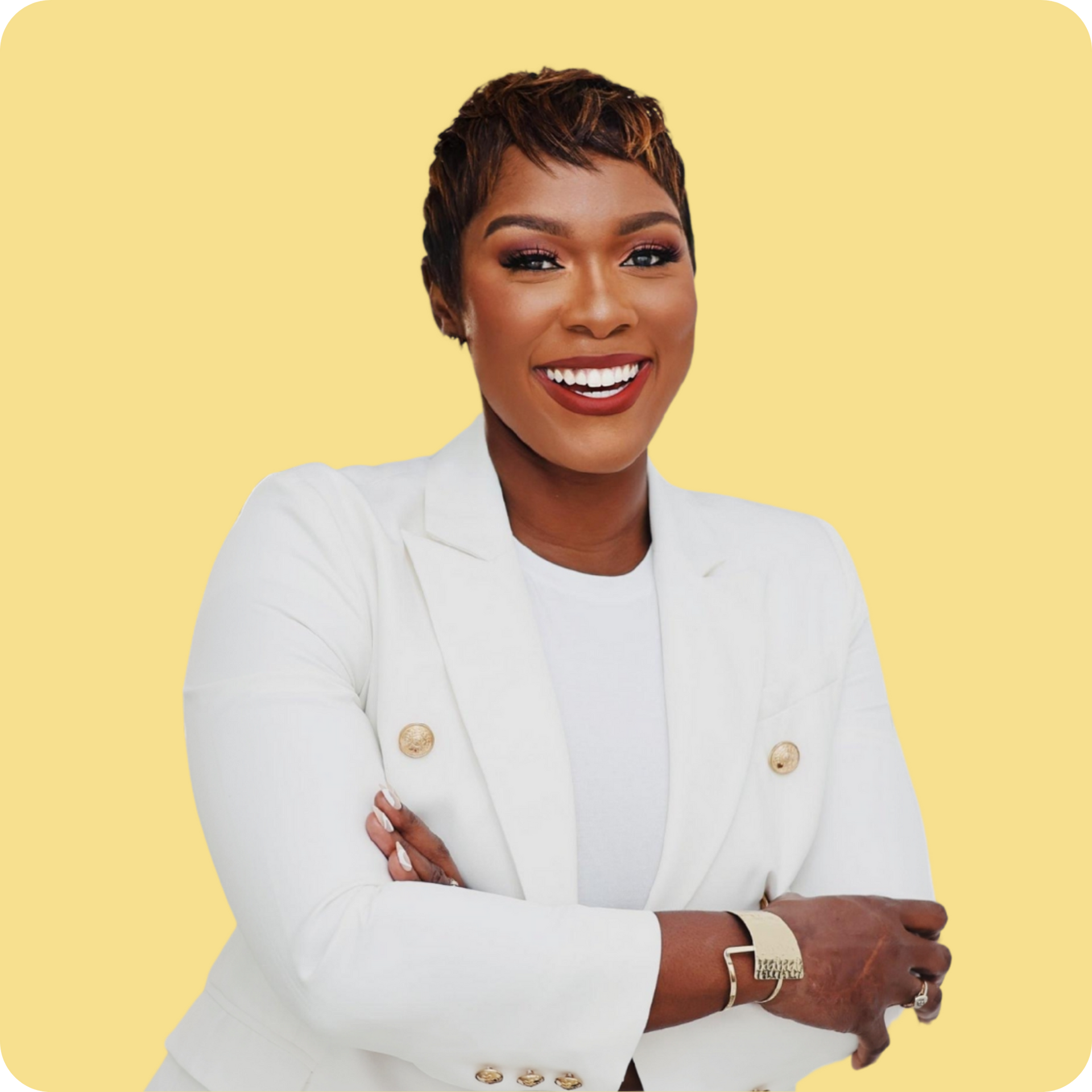 A Black woman smiling with her arms crossed. She is wearing white shirt and blazer with gold buttons and a gold watch.