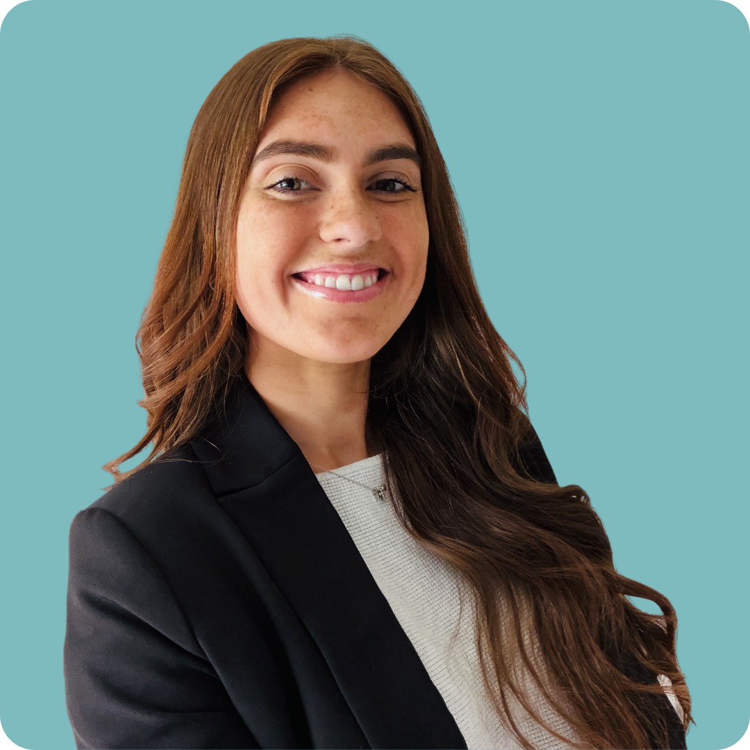 A woman with long brown hair and freckles is wearing a white shirt with black blazer and smiling for the camera.