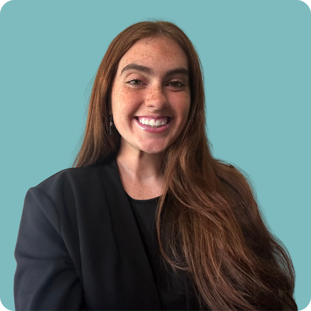 A woman with long brown hair and freckles is wearing a black blazer and smiling for the camera.