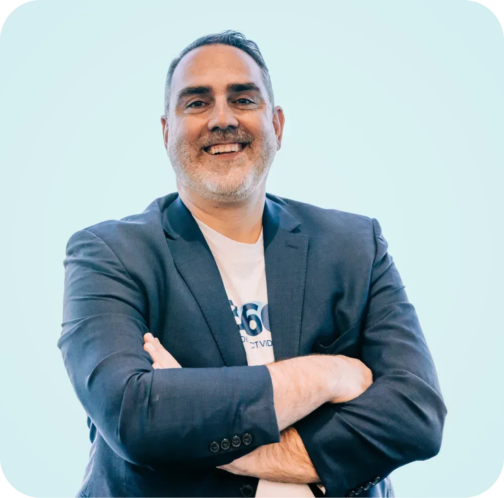 A man in a suit and white shirt is smiling with his arms crossed.