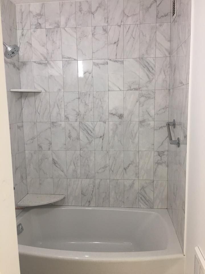 There is a bathtub in the shower with marble tiles on the wall.