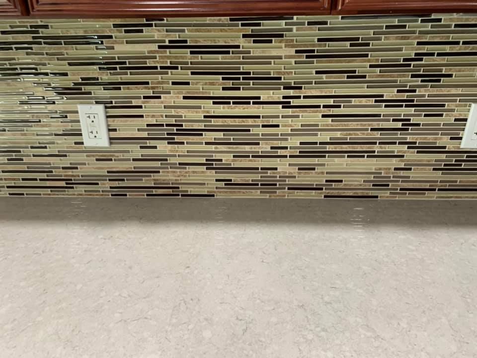 A kitchen counter with a tile wall and two electrical outlets.