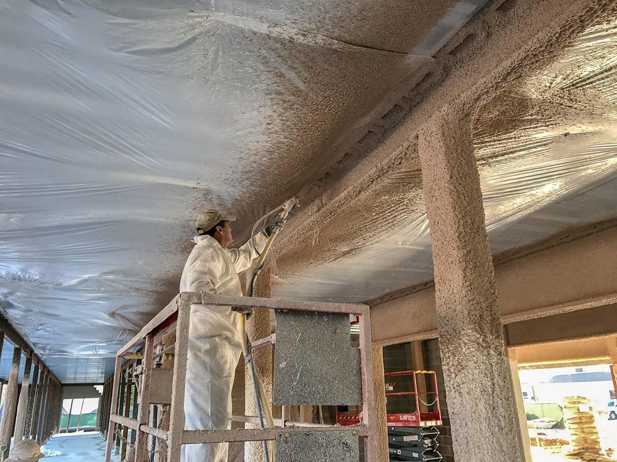 A man is spraying foam on the ceiling of a building.