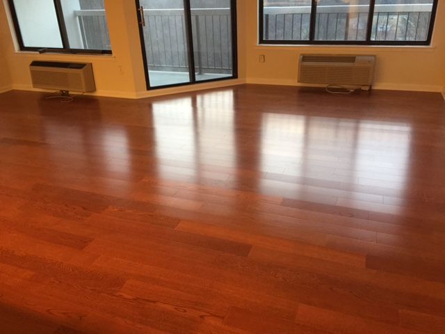 Polished reddish-brown hardwood floor reflecting light; windows and air conditioning units visible.