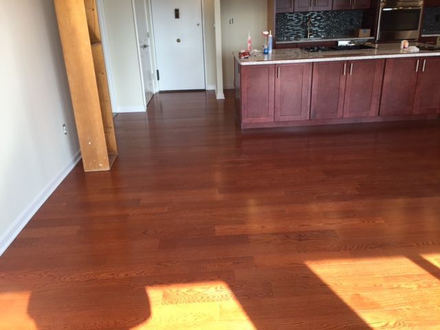 Hardwood floor in a kitchen, with wooden cabinets. Sunlight streams in.