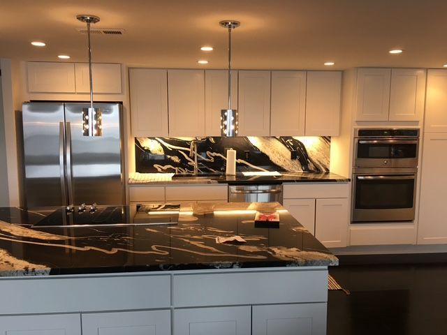 Modern kitchen with white cabinets, stainless steel appliances, black and white marble countertops, and pendant lights.
