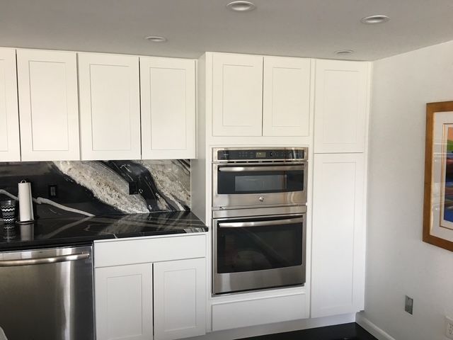 White kitchen cabinets with stainless steel oven/microwave, black and white countertops.