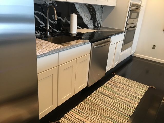 Kitchen with white cabinets, stainless steel appliances, black countertop, and rug.