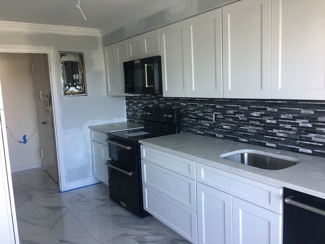 White kitchen with black appliances and backsplash, grey countertops, and a light tile floor.