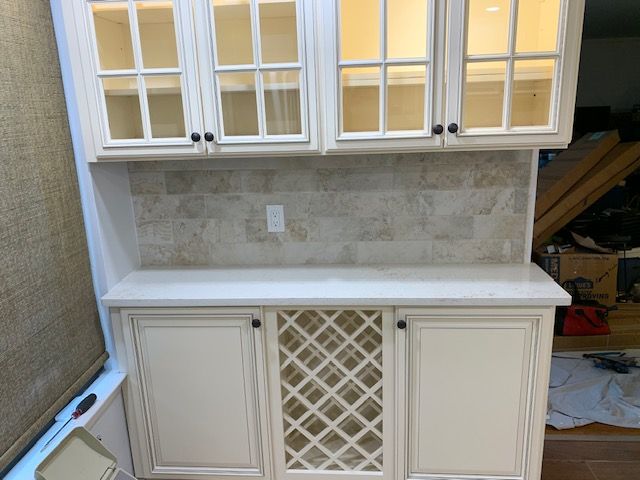 White kitchen cabinetry with glass-front uppers, tile backsplash, and a countertop with a wine rack.