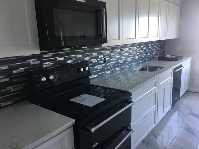 Modern kitchen with white cabinets, black appliances, and gray countertops, tiled backsplash.